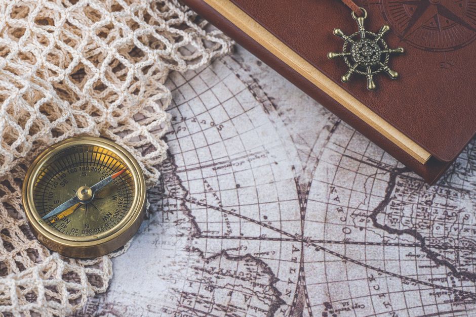 Flat lay of a vintage compass and leather notebook on a retro maritime map.