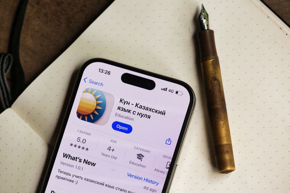 Smartphone displaying a language learning app next to a vintage pen on a notebook.