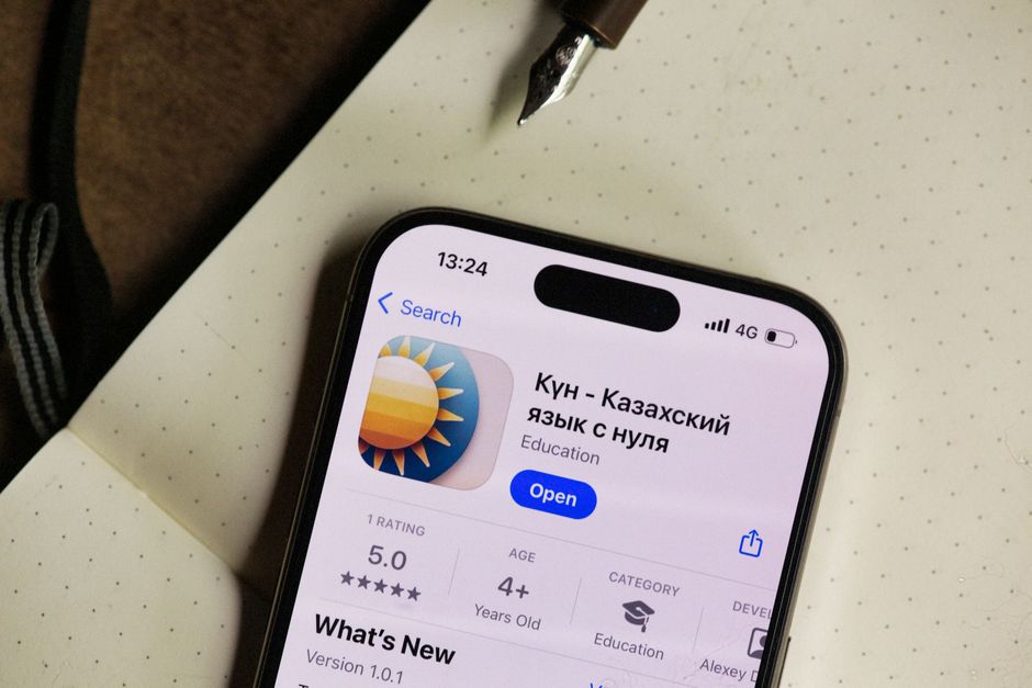 Close-up of a smartphone screen showing a Kazakh language learning app in an open notebook setting.
